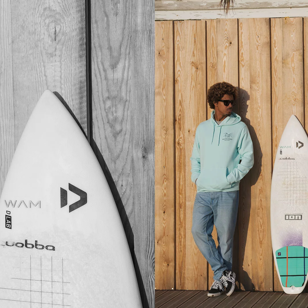 fotografía de Matchu Lopes con la sudadera de Made in Tarifa, con el diseño de Valdevaqueros en un color azul mar y una tabla de kitesurf